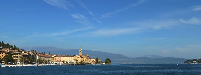 Trip Kosovo beliebte Urlaubsziele am Gardasee -  Mit einer Fläche von 370 km² ist der Gardasee der größte See Italiens. Es liegt am Fuße der Alpen und erstreckt sich über drei Staaten: Lombardei, Venetien und Trentino. Die maximale Tiefe des Sees beträgt 346 m, er hat eine längliche Form und sein nördliches Ende ist sehr schmal. Dort ist der See von den Bergen der Gruppo di Baldo umgeben. Du trittst aus deinem gemütlichen Hotelzimmer und es begrüßt dich die warme italienische Sonne. Du blickst auf den atemberaubenden Gardasee, der in zahlreichen Blautönen schimmert - von tiefem Dunkelblau bis zu funkelndem Türkis. Majestätische Berge umgeben dich, während die Brise sanft deine Haut streichelt und der Duft von blühenden Zitronenbäumen deine Nase kitzelt. Du schlenderst die malerischen, engen Gassen entlang, vorbei an farbenfrohen, blumengeschmückten Häusern. Vereinzelt unterbricht das fröhliche Lachen der Einheimischen die friedvolle Stille. Du fühlst dich wie in einem Traum, der nicht enden will. Jeder Schritt führt dich zu neuen Entdeckungen und Abenteuern. Du probierst die köstliche italienische Küche mit ihren frischen Zutaten und verführerischen Aromen. Die Sonne geht langsam unter und taucht den Himmel in ein leuchtendes Orange-rot - ein spektakulärer Anblick.